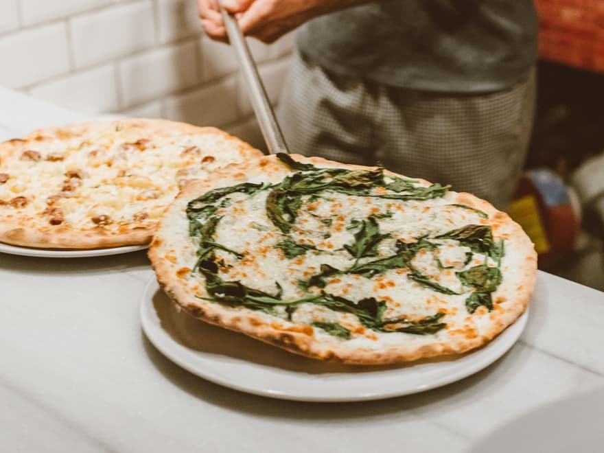 Pizza maker sliding fresh pizzas onto plates